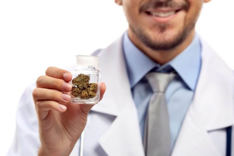 A person in a lab coat holding a small jar of marijuana