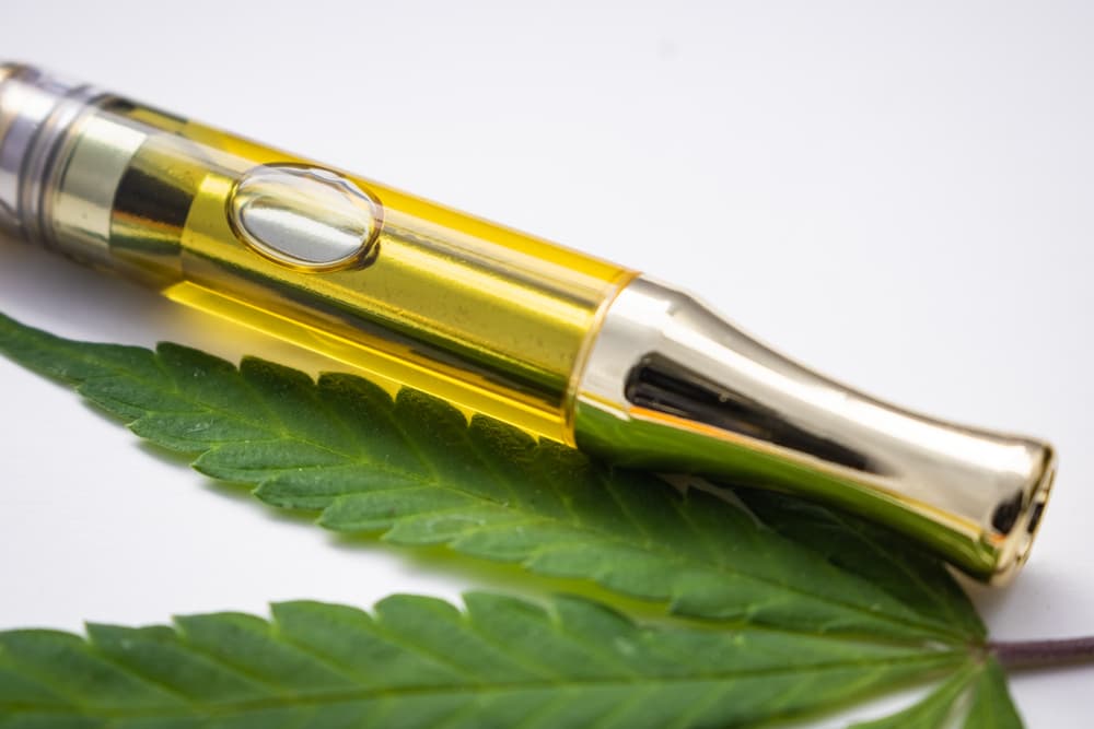 Cannabis Extracted Oil Distillate In Vape Pen Cartridge Up Close With Hemp Leaf